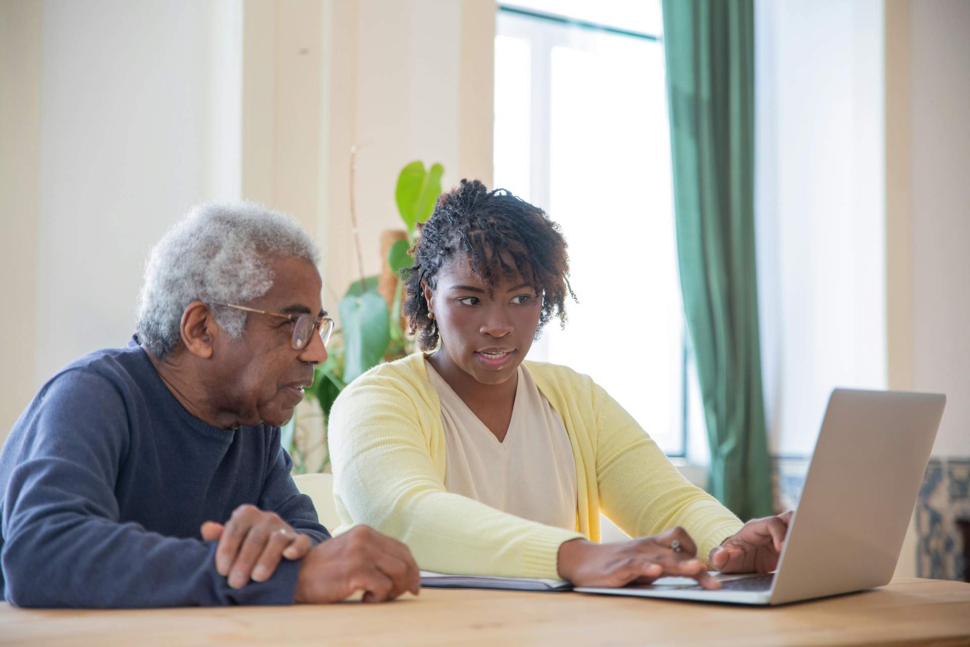 Caregiver teaching elderly man how to work on a laptop